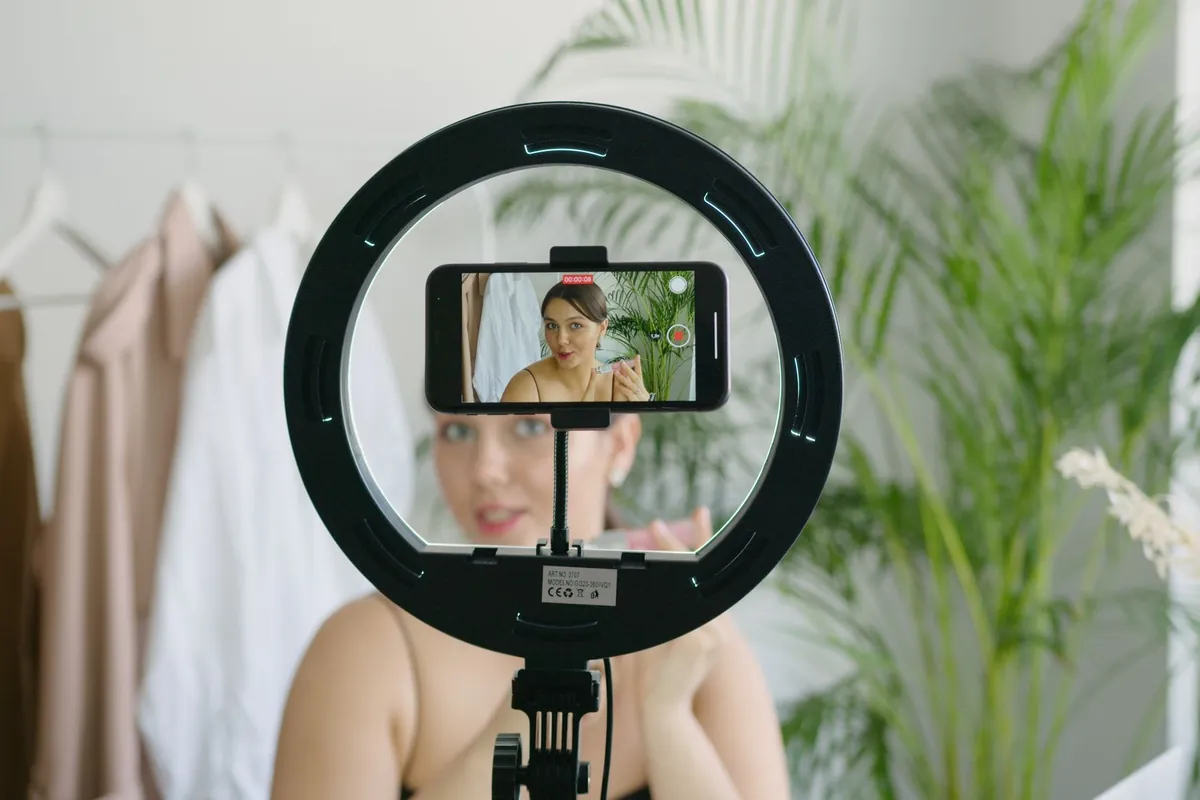 Woman recording a video of herself on a smartphone mounted in a ring light indoors
