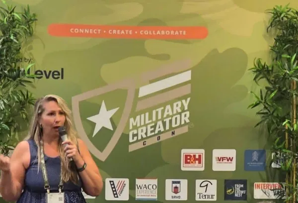 Trish Leto speaking into a microphone in front of the Military Creator Con backdrop